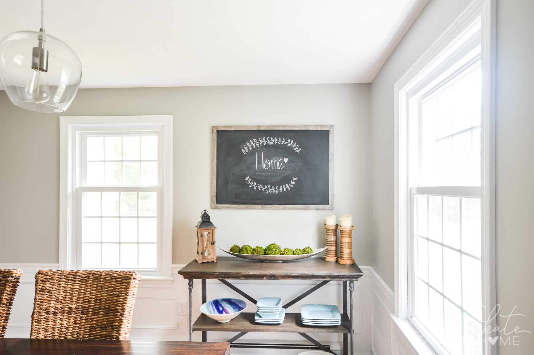 A corner of the dining room with a blackboard displaying chalk art and a side table with various decor items and extra plates/bowls