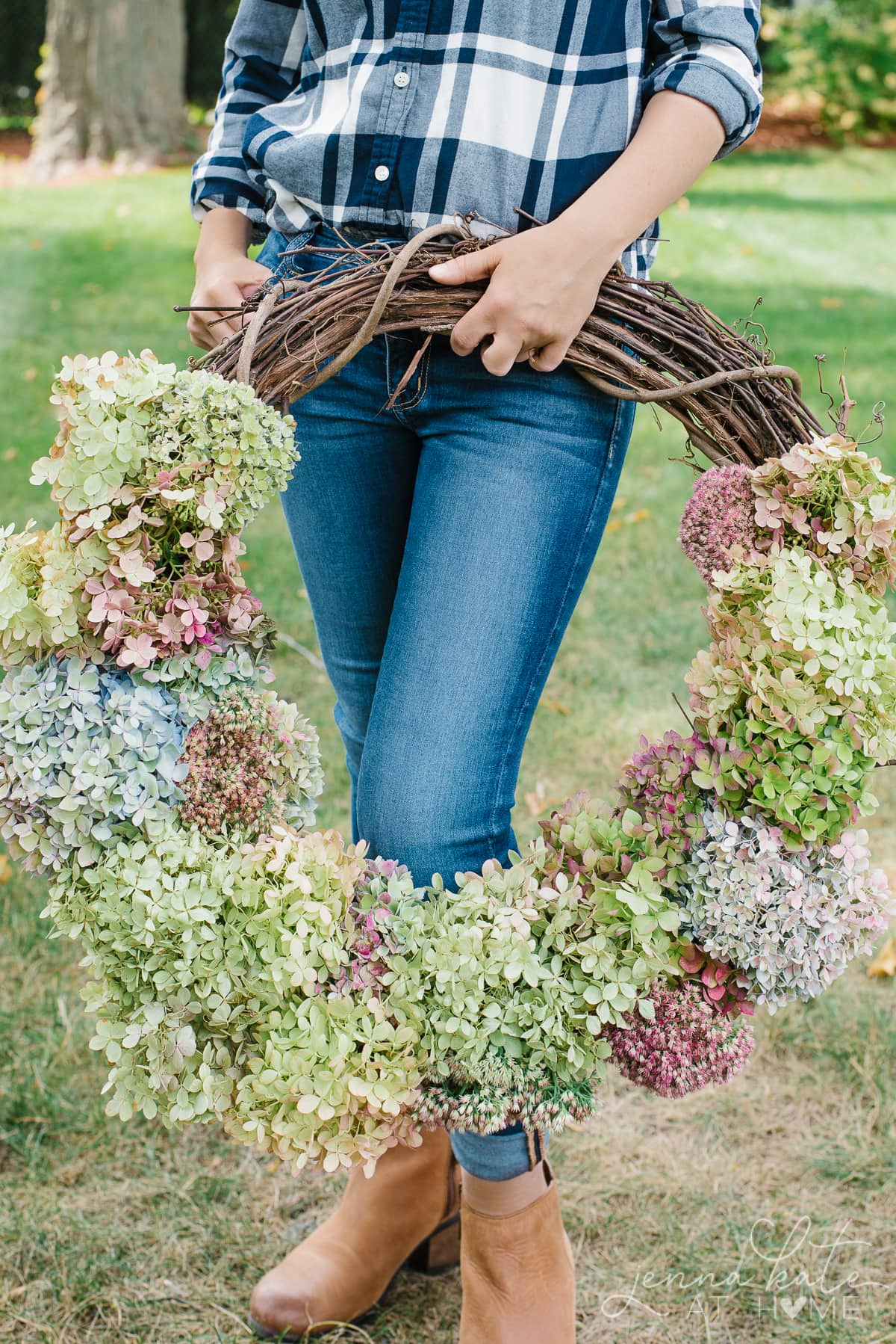 A person is standing in the grass holding a homemade hydrangea wreath