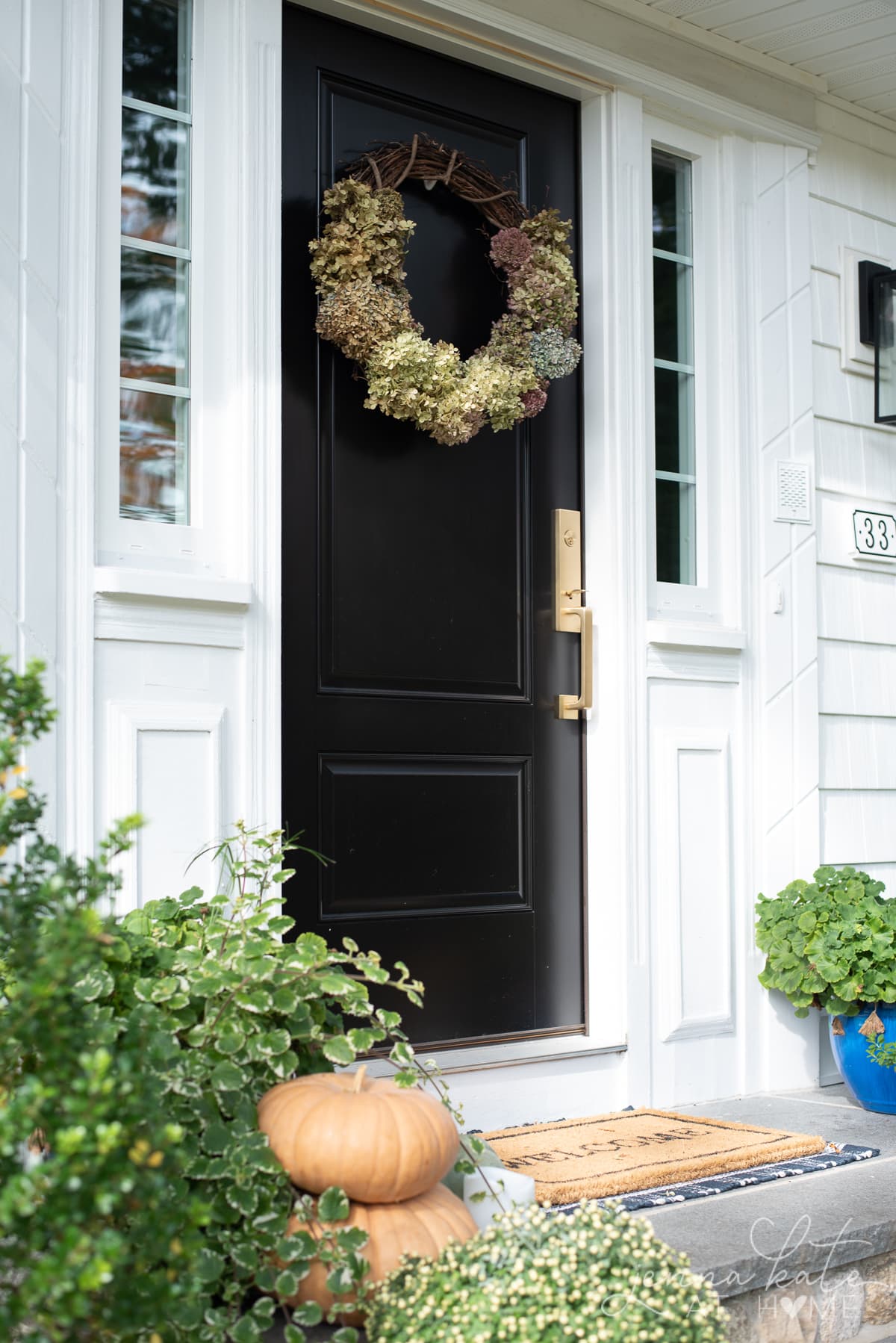 Dried hydrangea wreath on front door with pumpkins and mums on the front steps