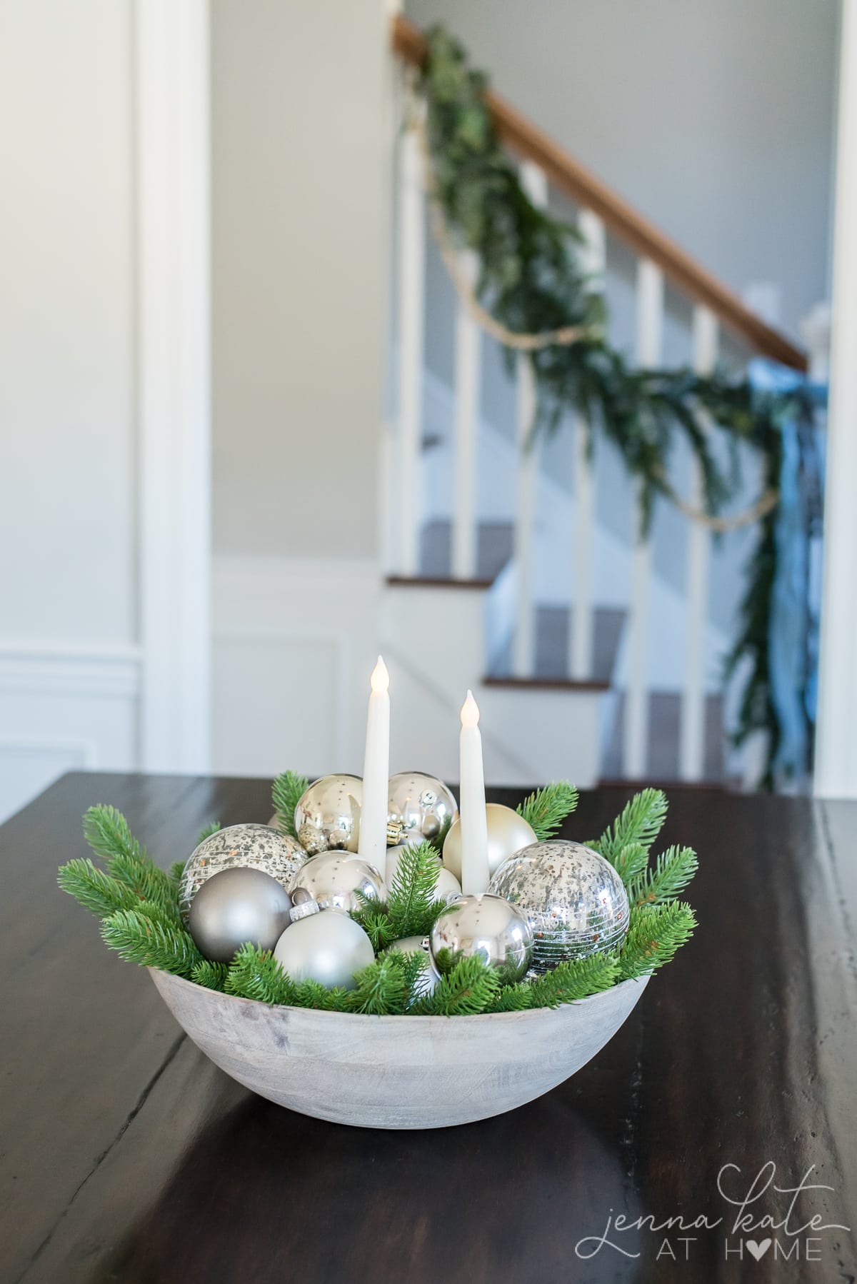 A bowl filled with greenery and ornament balls, with 2 battery operated candle in the middle