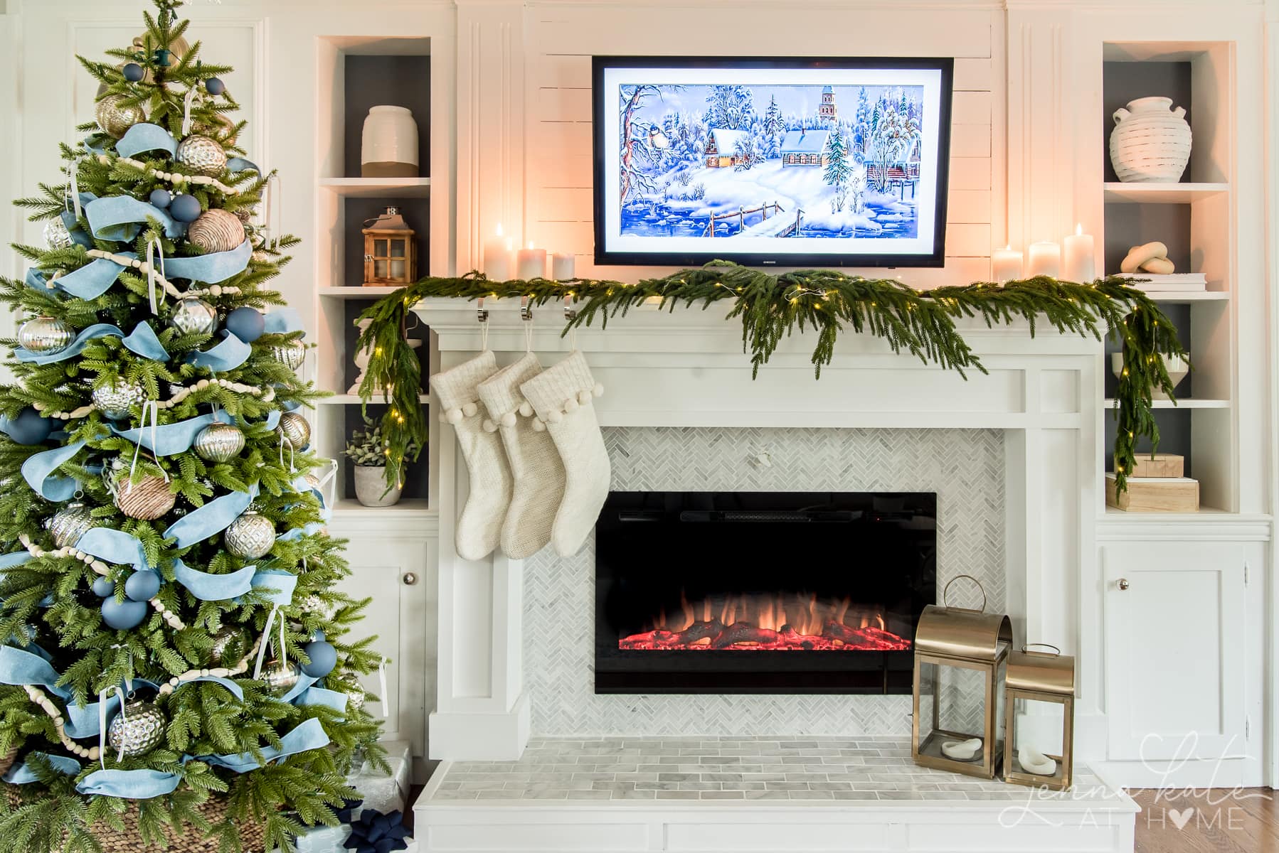 A Christmas mantel with white and cream stockings and greenery down the top. A faux Christmas tree wrapped with blue ribbon and blue and gold ornaments.