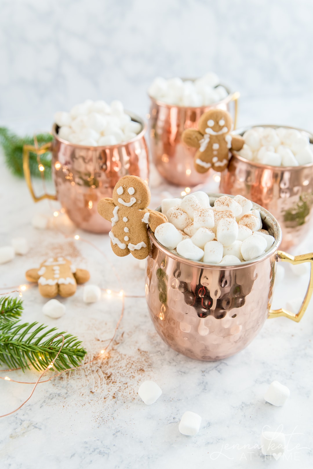 Copper mugs filled with gingerbread hot chocolate and marshmallows with a gingerbread man mug buddy