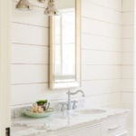 White shiplap adorns a small powder room wall, with large mirror and white sink below