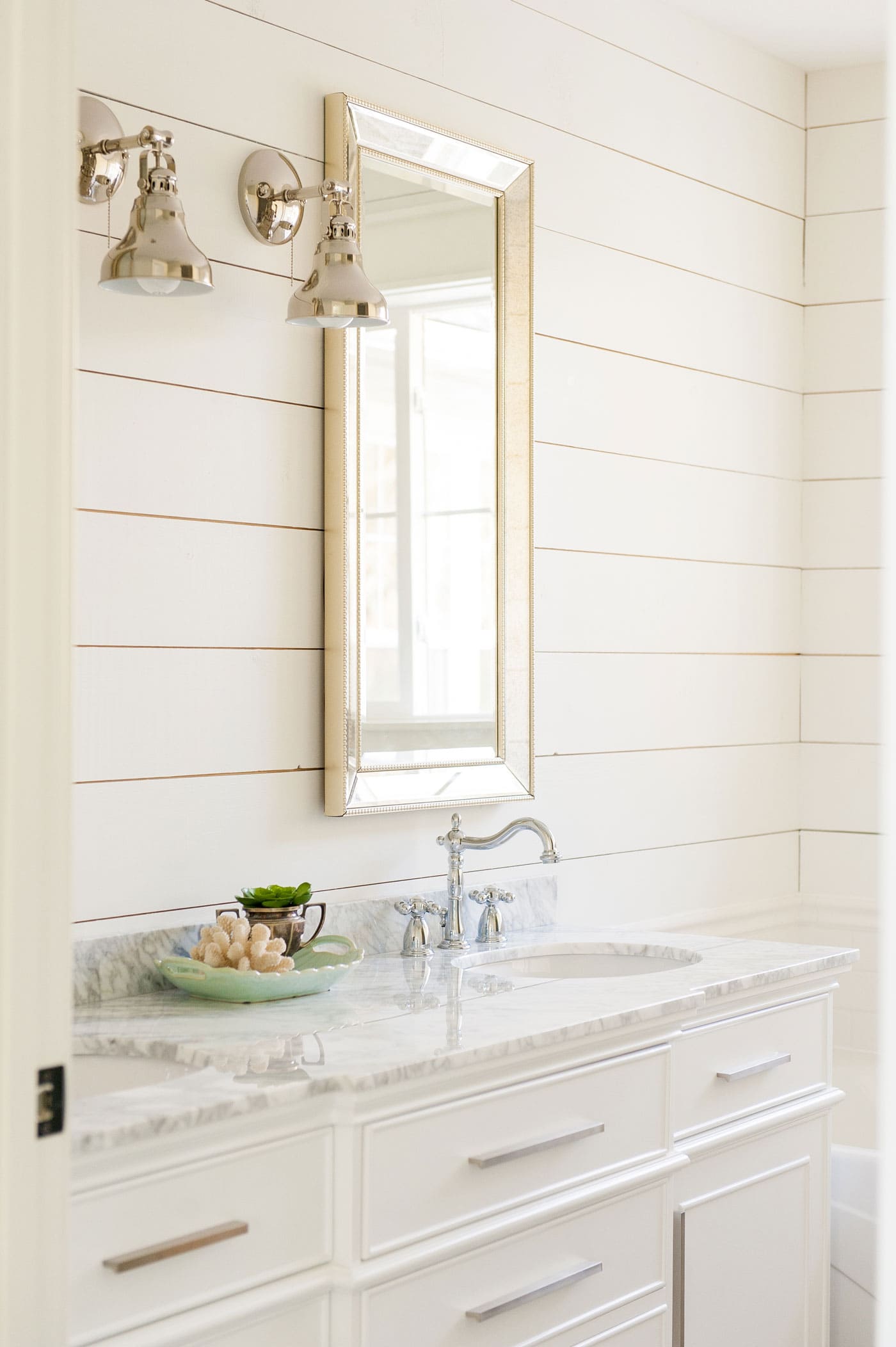 White shiplap adorns a small powder room wall, with large mirror and white sink below