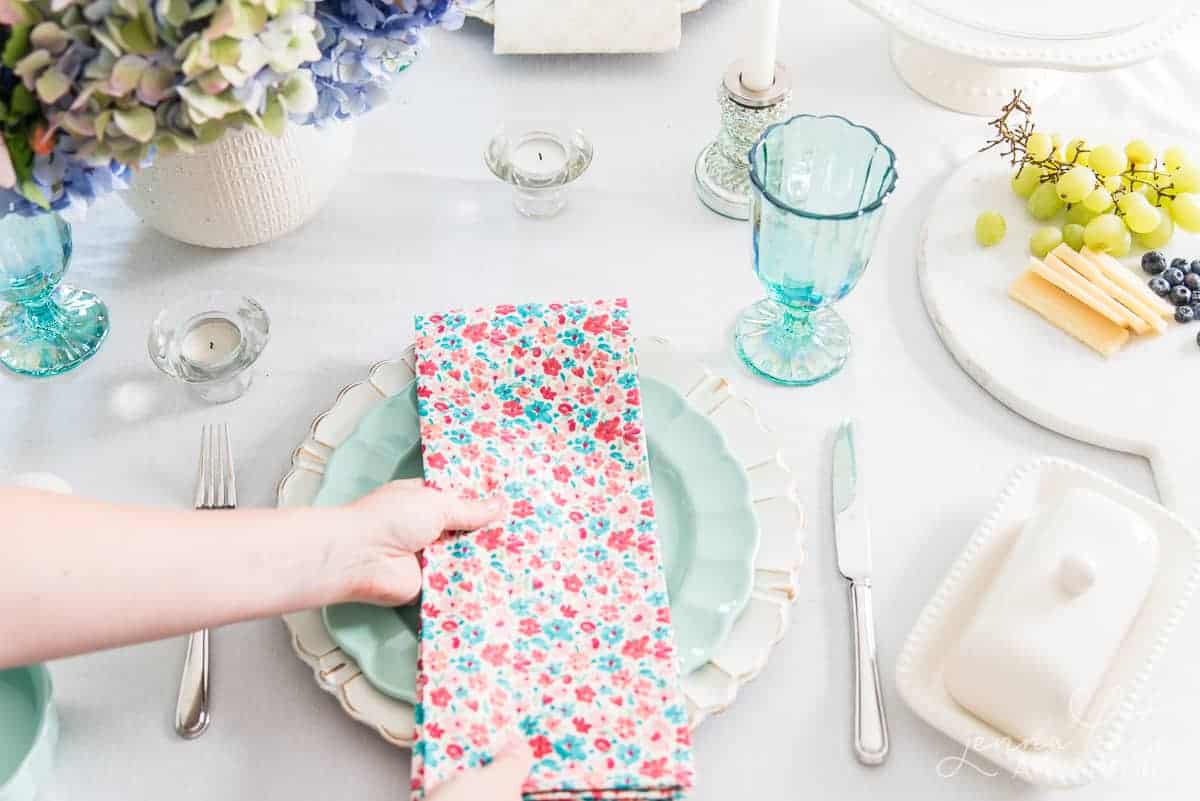 hand placing a floral napkin on a green plate as part of a spring table setting