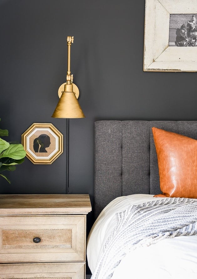 Iron Ore accent wall with slate gray headboard and leather pillow on the bed and a gold wall sconce. 