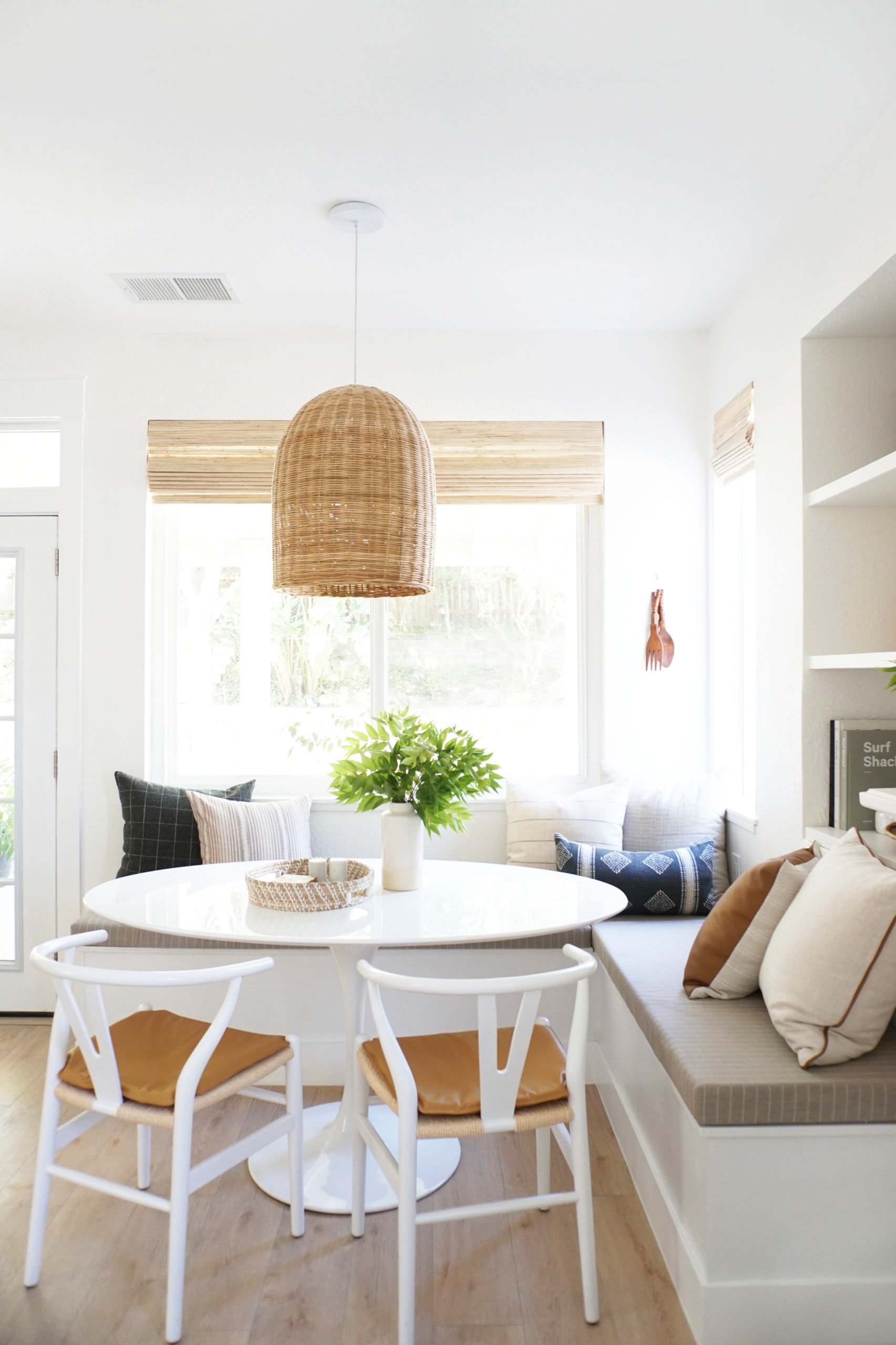 coastal style breakfast nook with large rattan pendant, upholstered bench and white tulip table