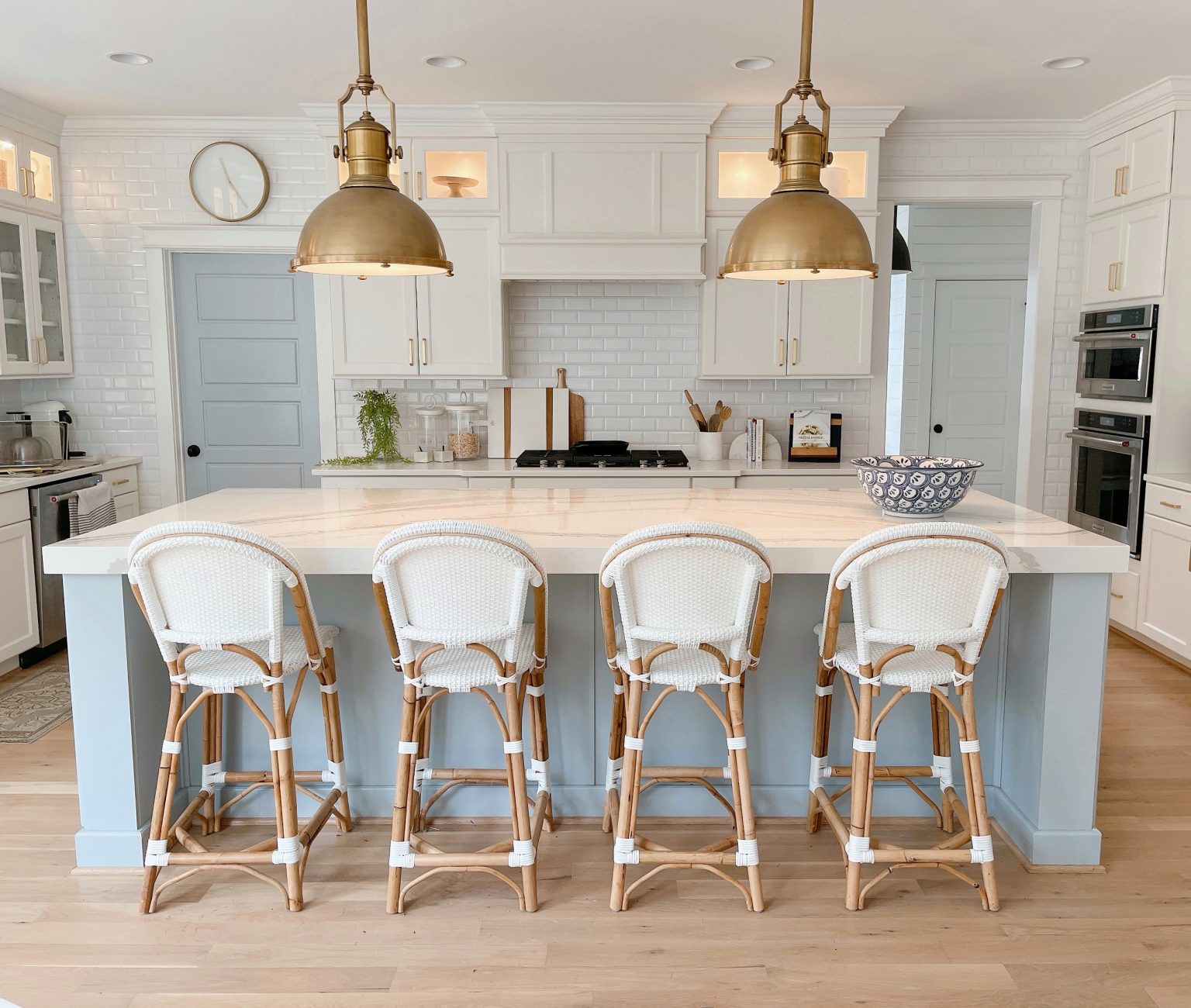 light blue kitchen island with white rattan counter stools and large brass pendants 