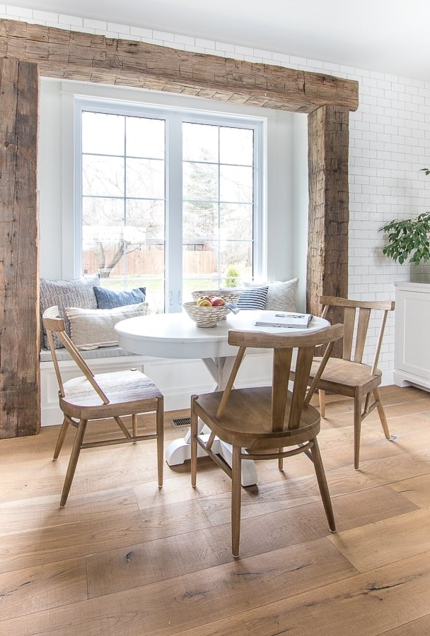 Recessed window framed out with chunky reclaimed wood beams and a white table and upholstered bench for the breakfast nook