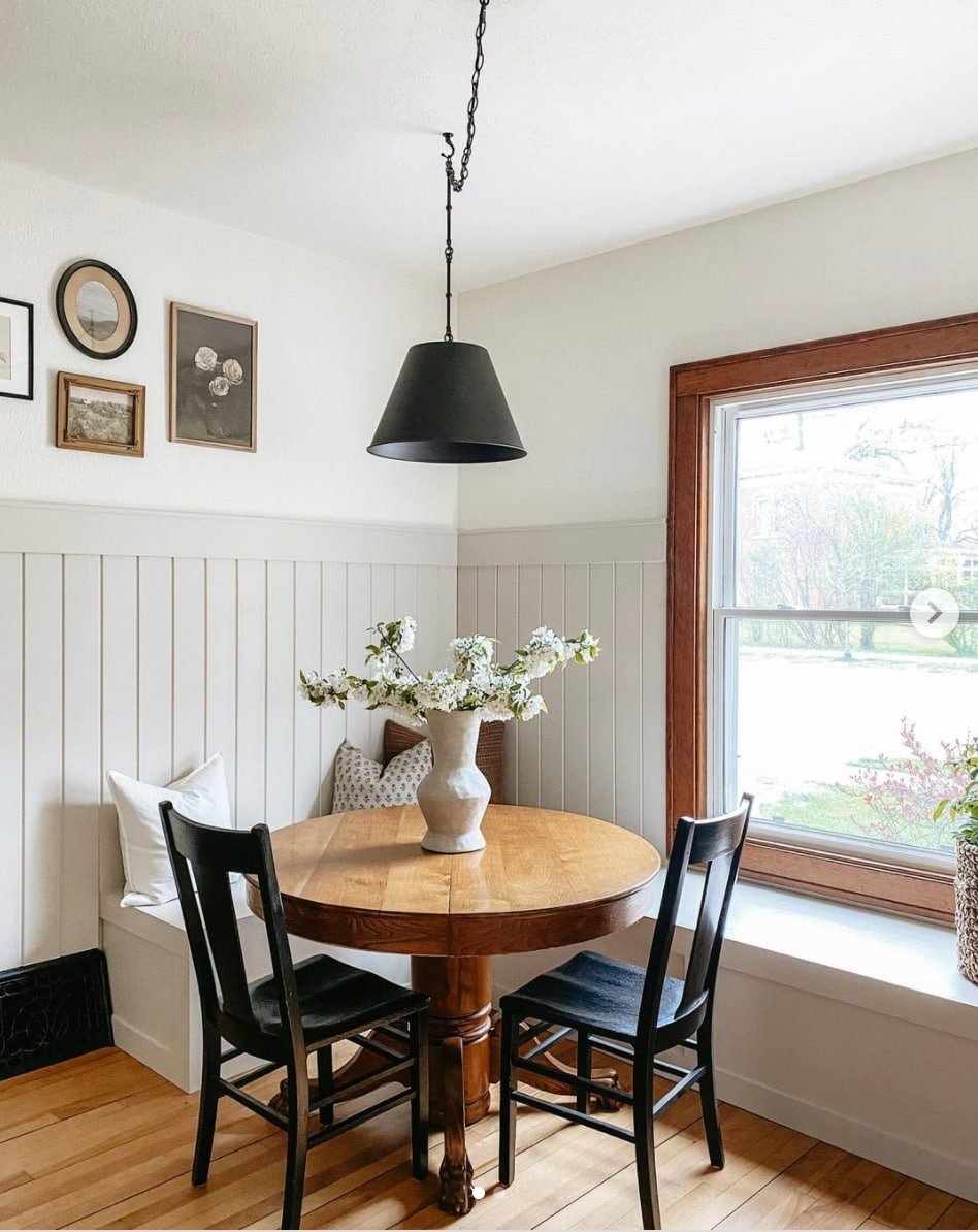 Wainscoting in cozy kitchen nook painted Sherwin Williams Accessible Beige with bench seating and chairs around a rounded wood table.