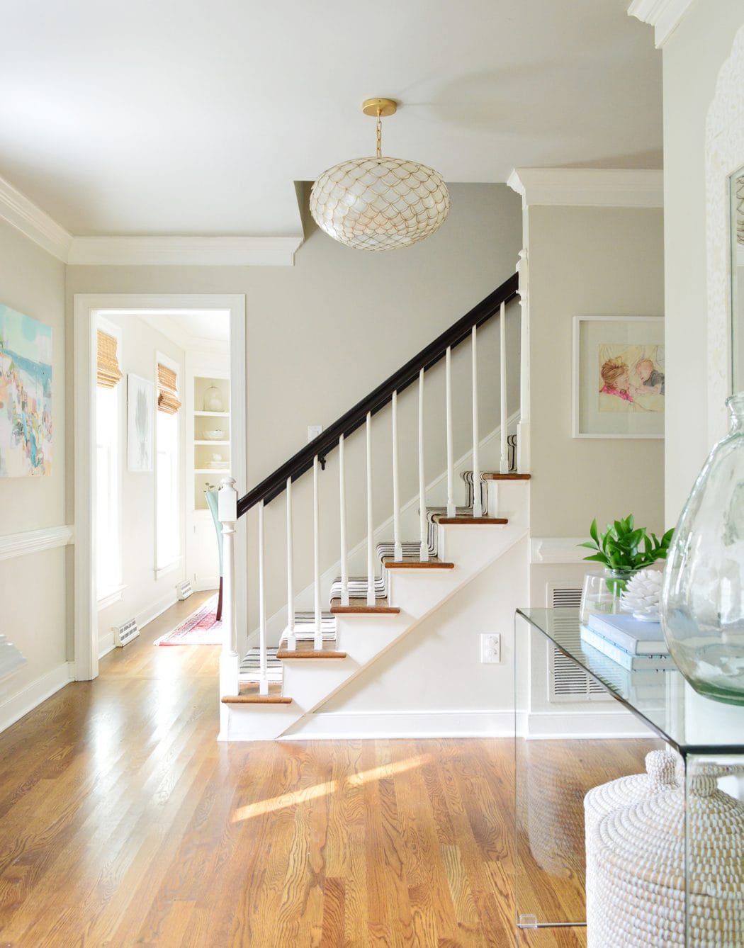Large, bright foyer painted with Benjamin Moore Edgecomb Gray with a beautiful gold, round light fixture next to the staircase.