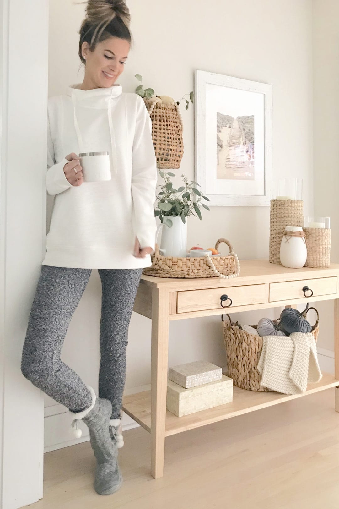 woman standing next to light wood console table with the background wall painted classic gray