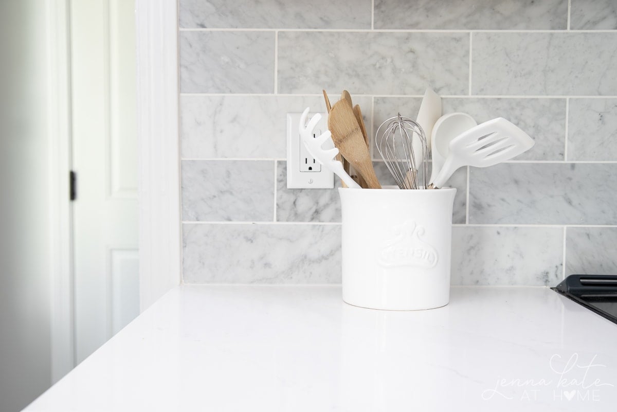 white kitchen countertop with marble backsplash and utensil crock