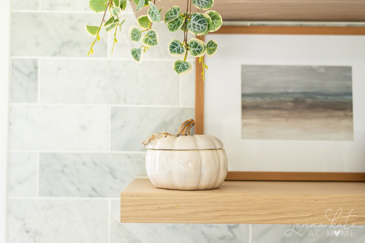 ceramic pumpkin and fall artwork on a floating shelf