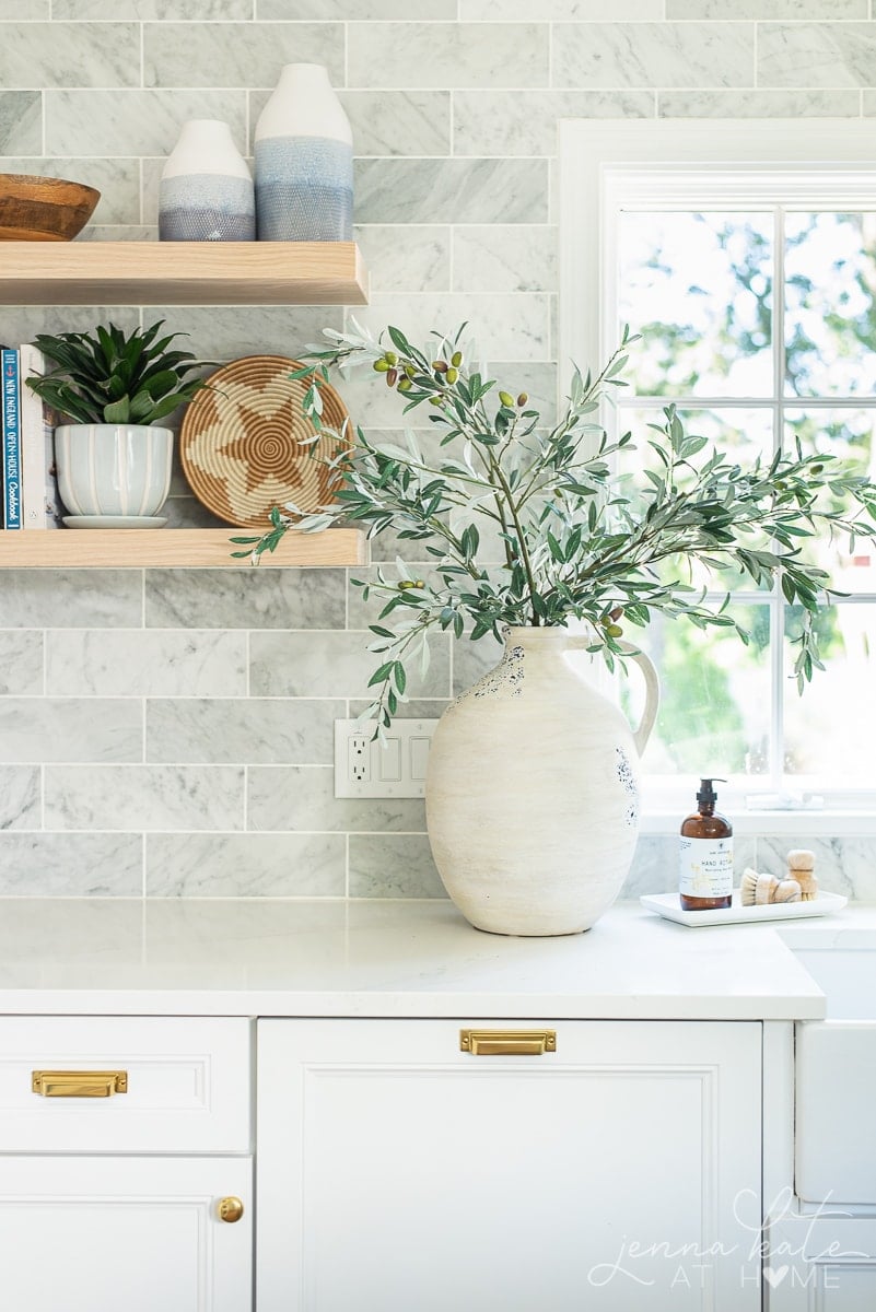 vase of faux olive branches next to kitchen sink.