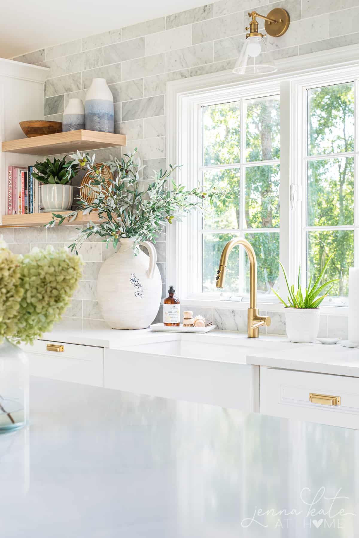kitchen window with a large vase next to the sink filled with olive branches