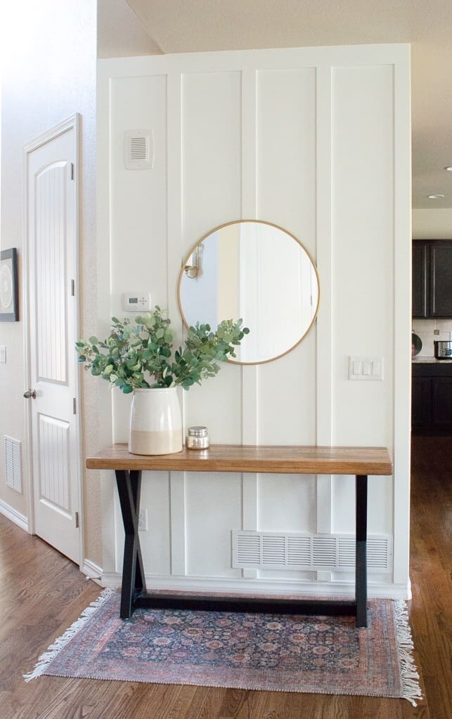 Vertical Paneled Entry Accent Wall 
 painted with Benjamin Moore Chantilly Lace. A simple wooden table with potted plant and round mirror.