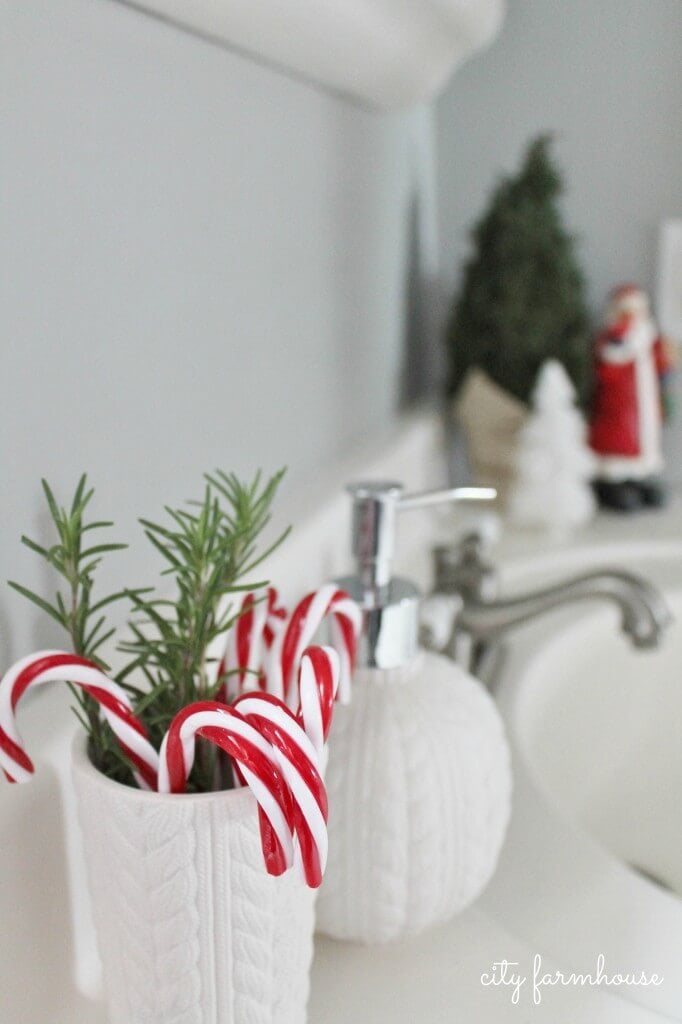 candy canes in a white cup with small Santa in the background