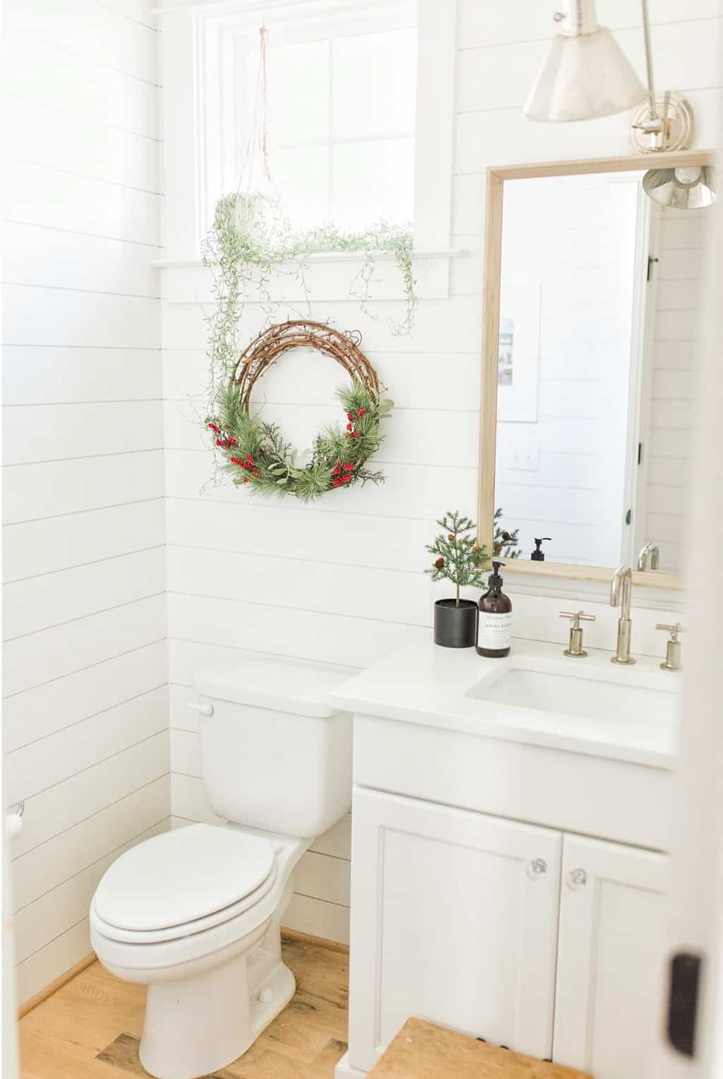 white small bathroom with christmas wreath over the toilet and tiny tree in vase on vanity