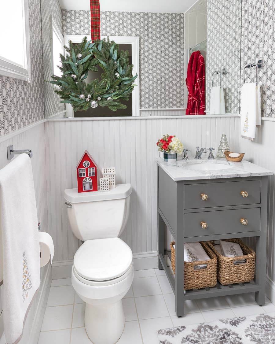 grey single vanity with red Christmas house on back of toilet and wreath over toilet