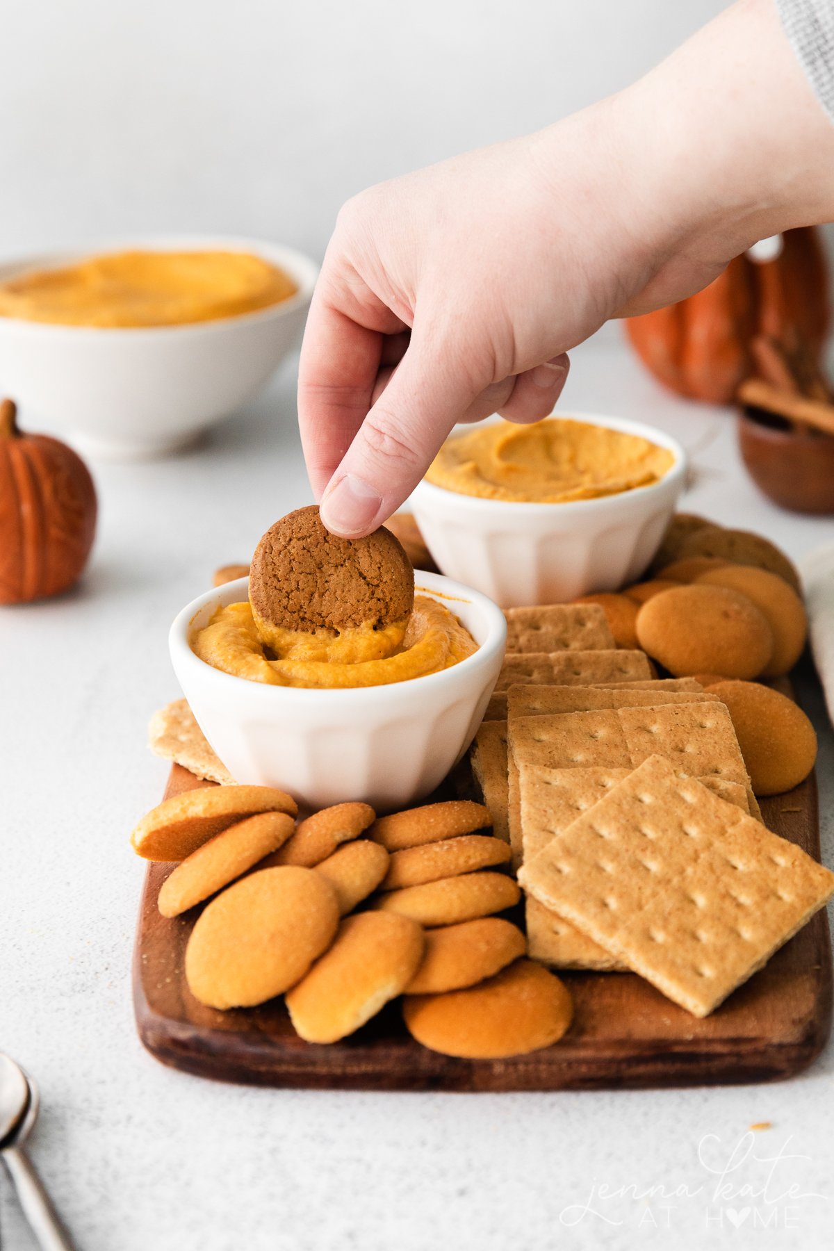 hand dipping a gingersnap cookie into the pumpkin cheesecake dip