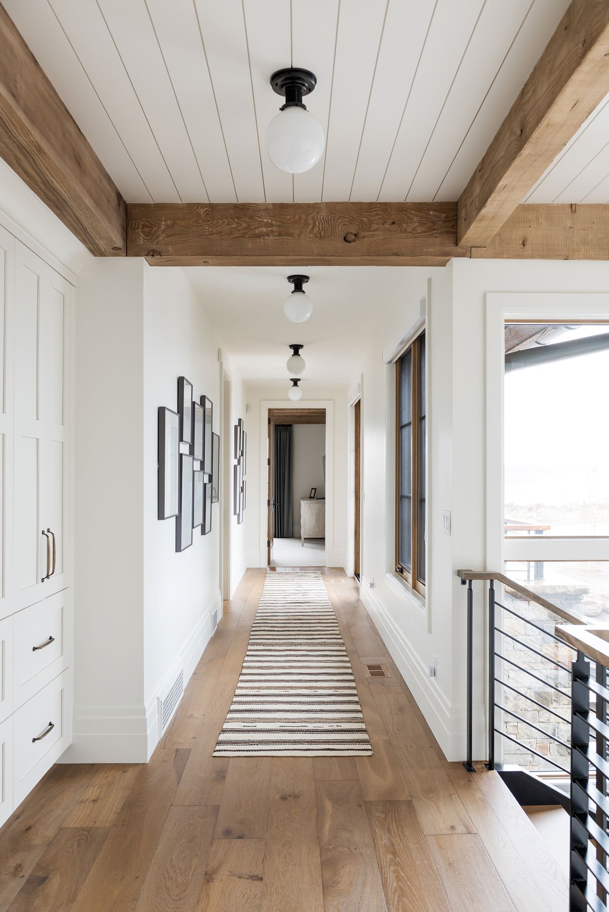 White walls in a hallway with wooden beams overhead and medium toned wood floors