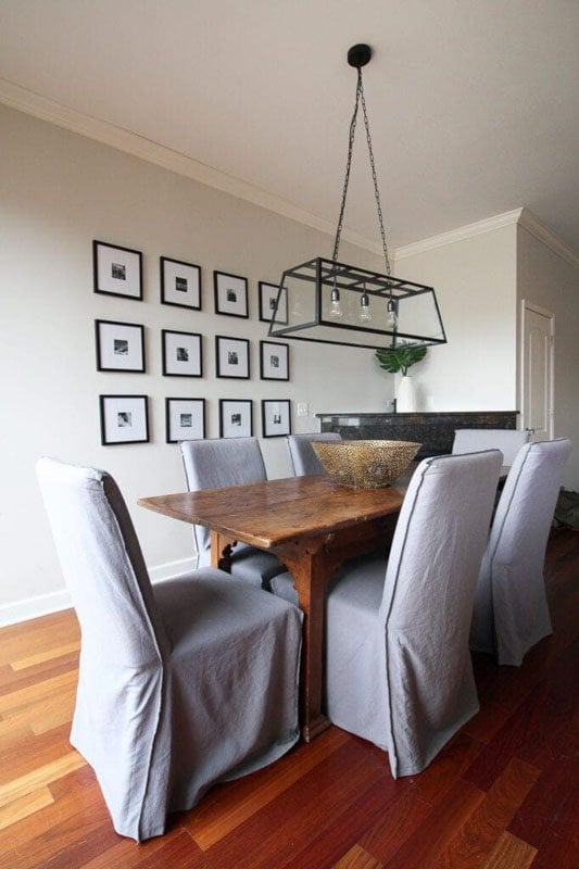 dining room with farmed photo gallery wall wood table grey covered dining chairs and metal industrial lighting above table 