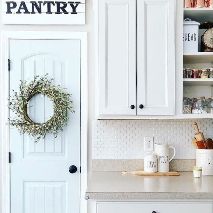 view of kitchen pantry door with pantry metal sign and white kitchen cabinets