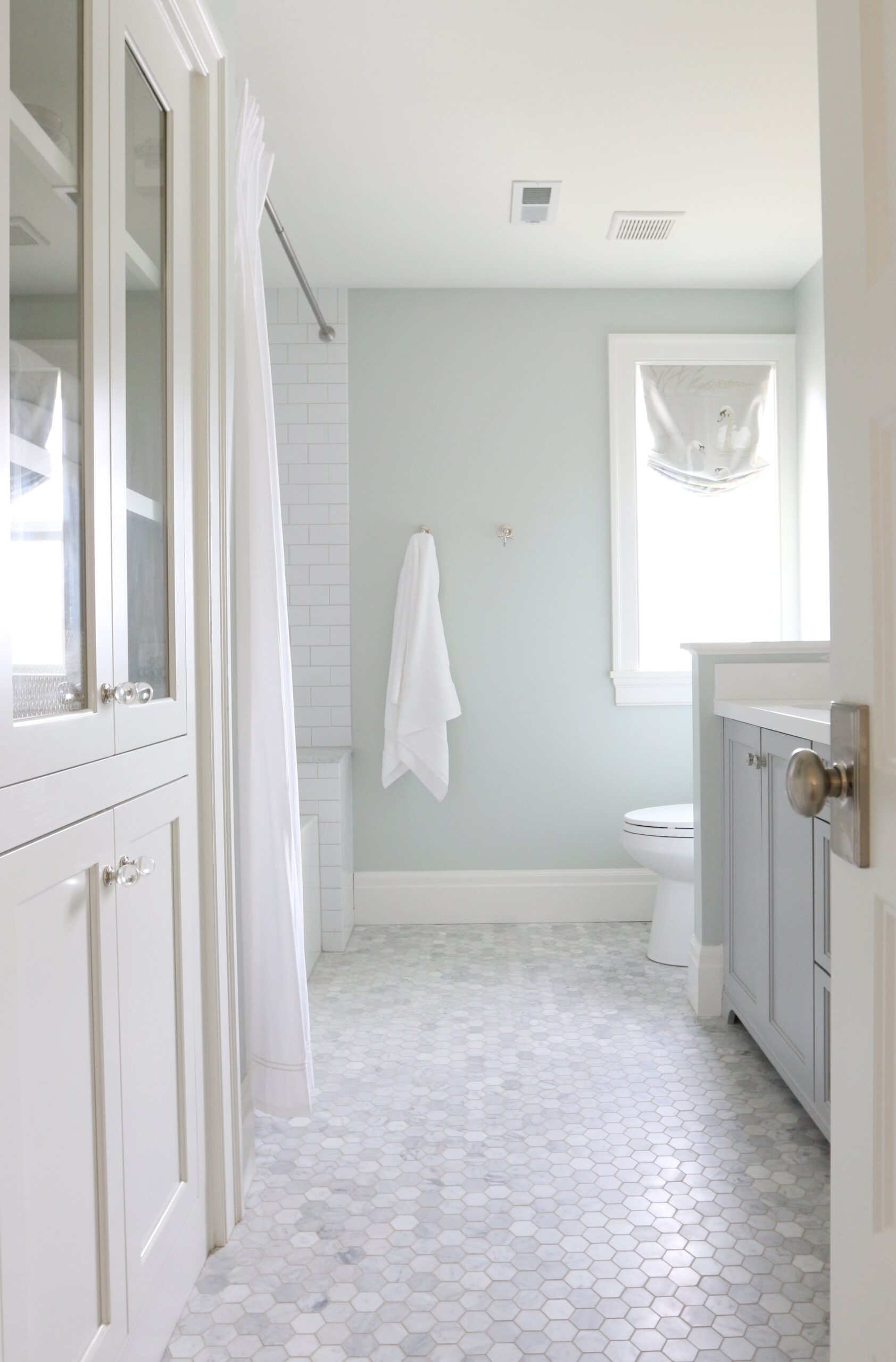 White bathroom with subway tile shower, tiled floors, green walls, window