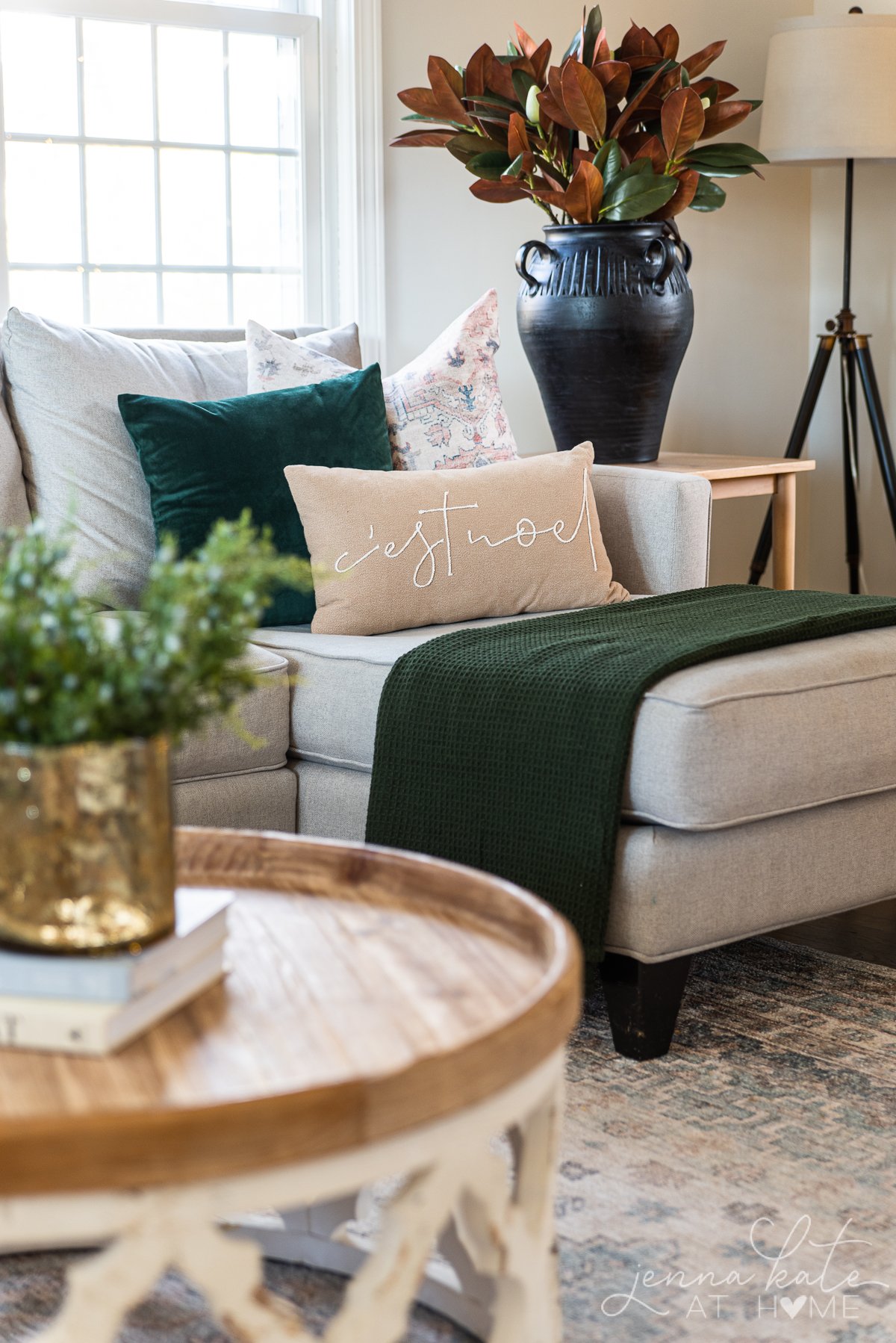 Black vase with magnolia branches and couch chaise with dark green throw pillow and blanket