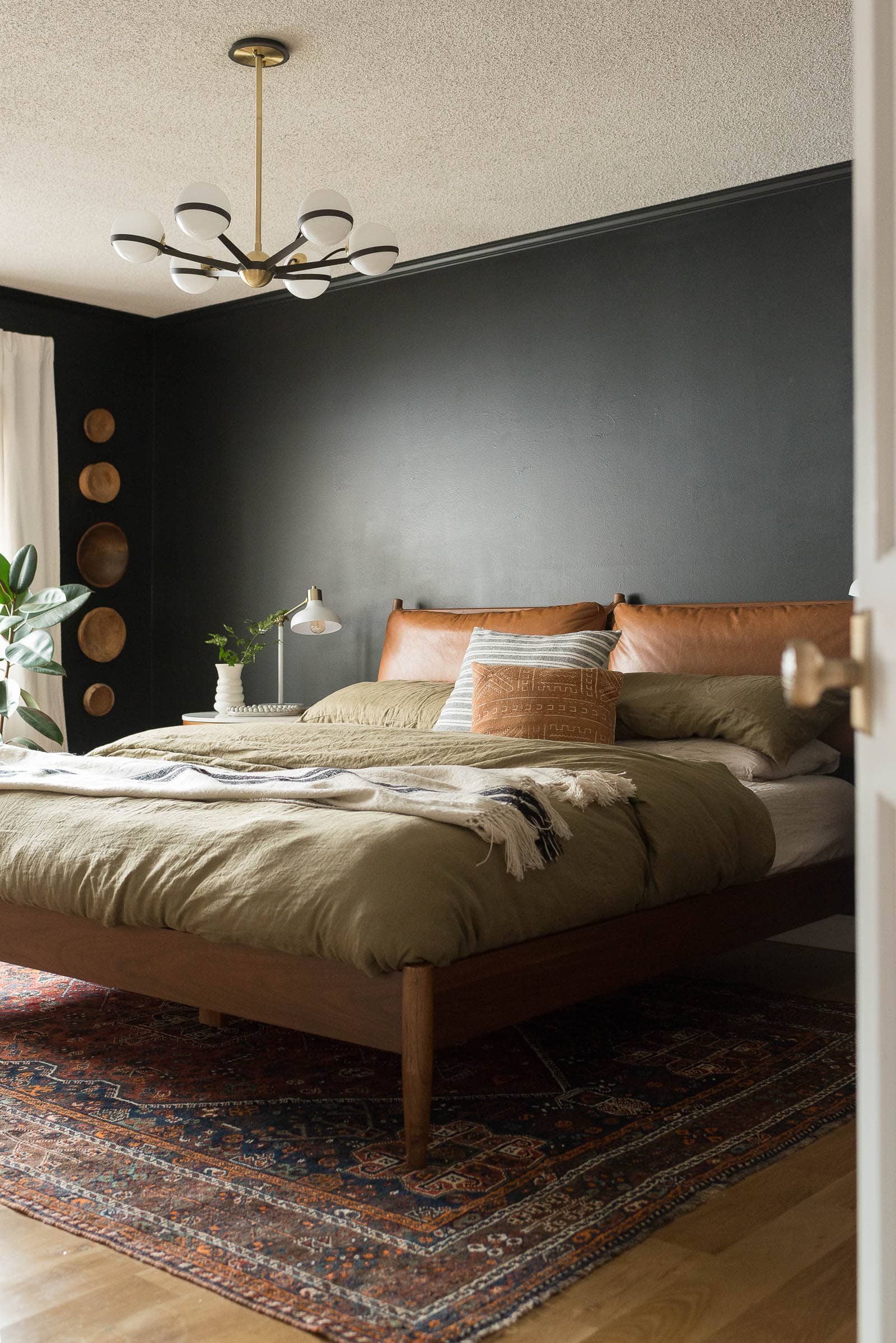 black bedroom with wood bed and tan pillows and neutral bedding