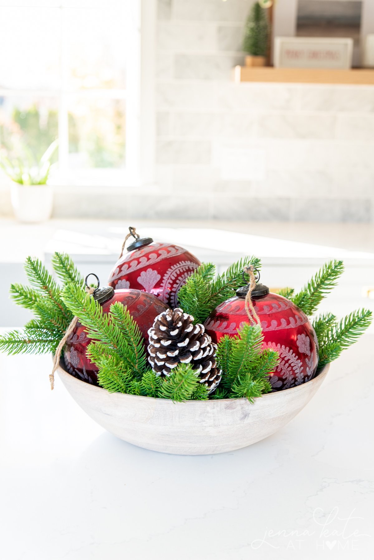 festive centerpiece filled with red glass ornaments and pinecones on a kitchen island