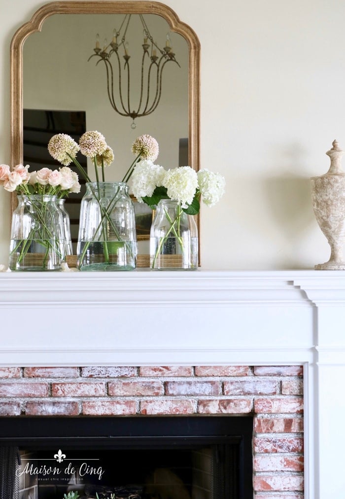simple white and brick fireplace mantel with glass vase and fresh blooms