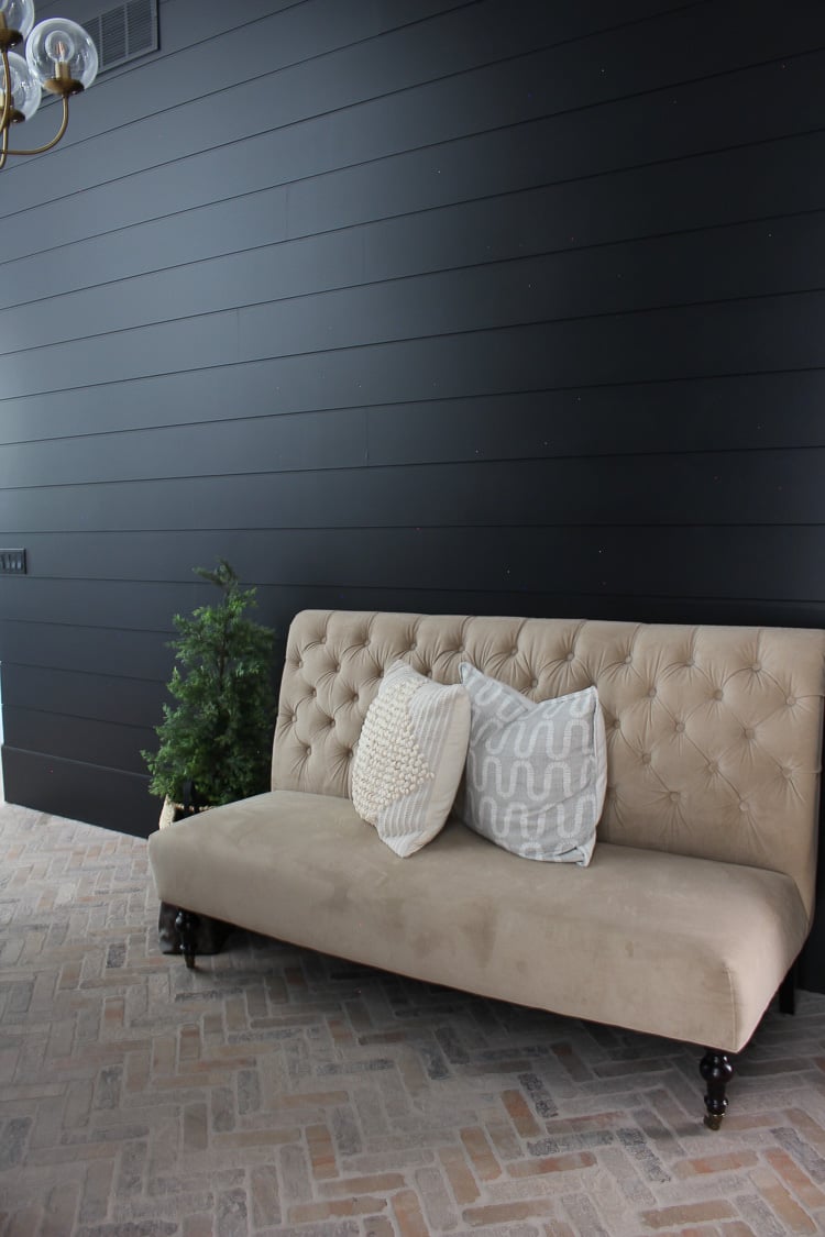 Tricorn Black shiplap wall with beige settee and brick flooring