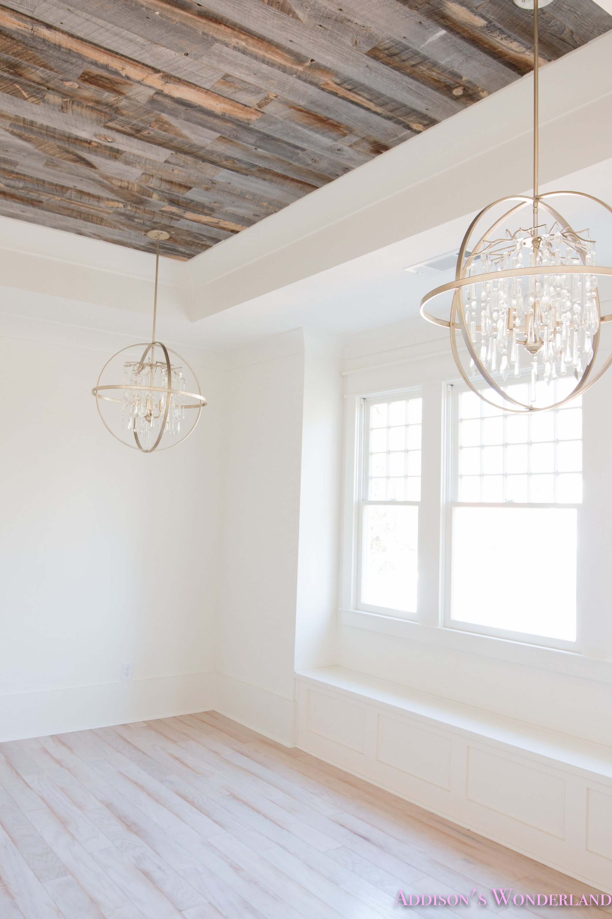 Empty bedroom walls painted Alabaster with distressed wood ceiling and two unique chandeliers hanging in front of the window.