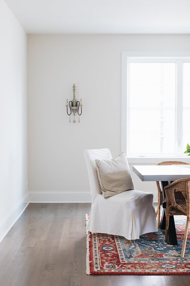 dining room with white slip covered chair, rust red rug and walls painted classic gray