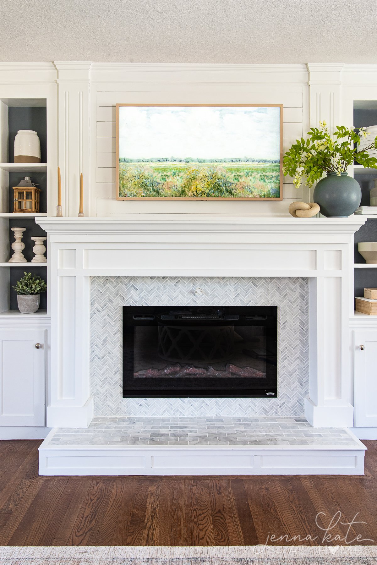 white fireplace with a frame TV with spring art above it and a vase filled with spring flowers.