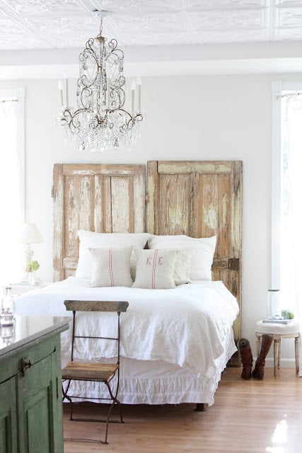 farmhouse bedroom decor vintage chippy doors used as headboard and white linens and glass bead chandelier