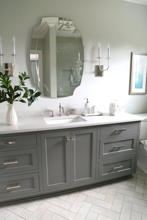 grey and white bathroom with white countertop, white herringbone flooring and grey cabinets