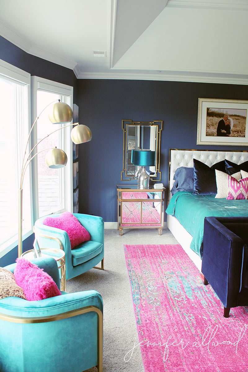 bedroom with dark blue walls, bright pink rug and turquoise accent chairs