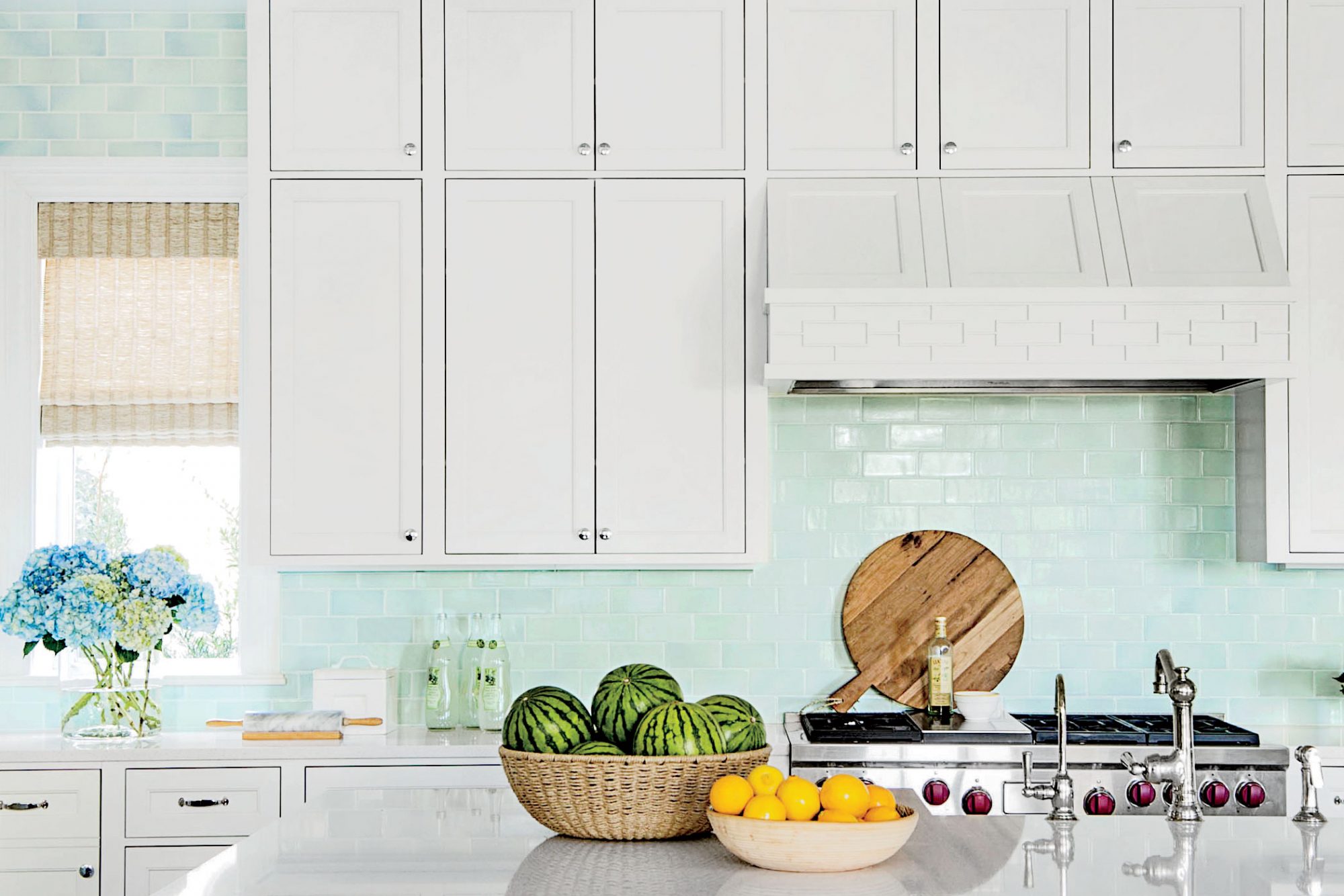 Sea blue glass kitchen backsplash with fruit on kitchen island and window on left