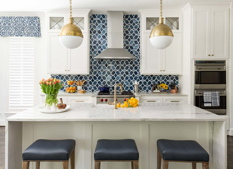 navy patterned kitchen backsplash tile with white cabinetry, double oven, kitchen island and rubbed bronze pendant lights