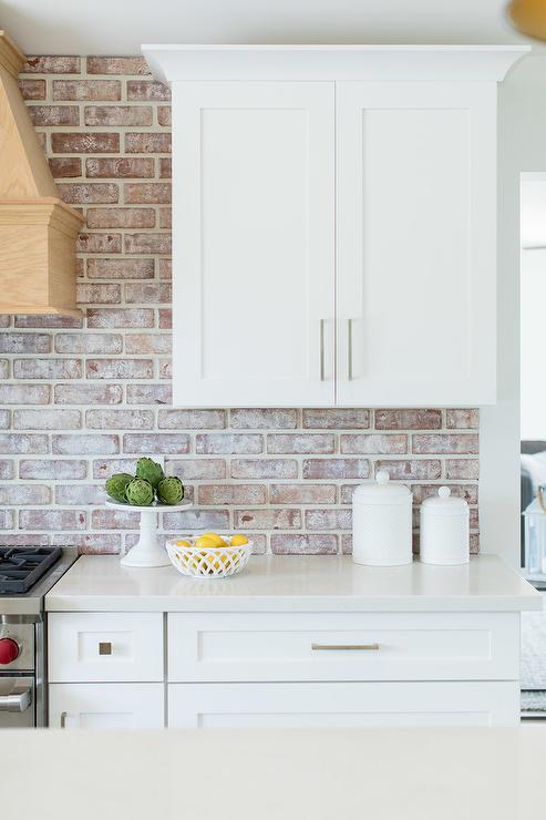 Whitewashed brick backsplash with white cabinets and wooden stove hood