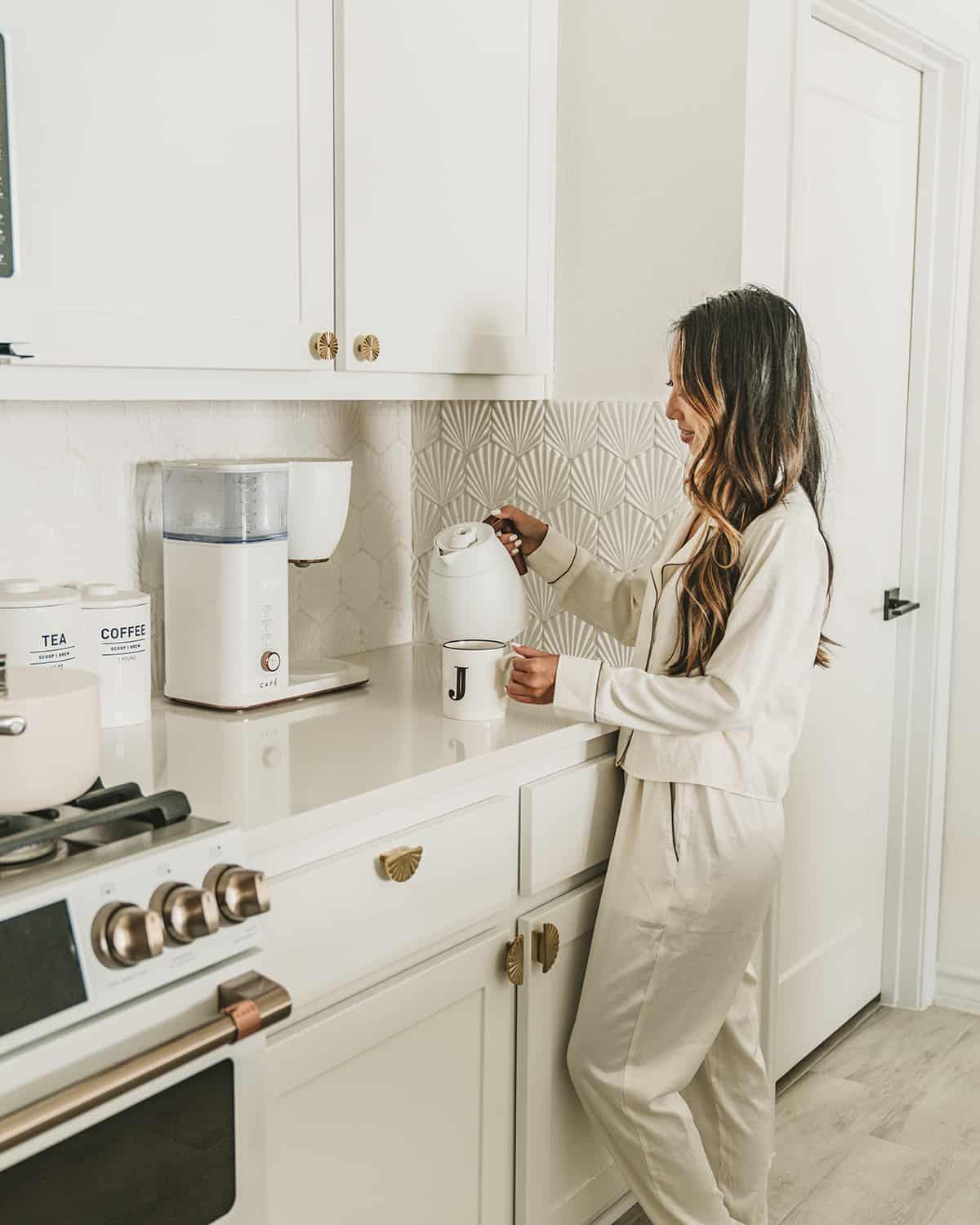 woman pouring coffee in kitchen, white cabinets with patterned and textured seashell white tile backsplash
