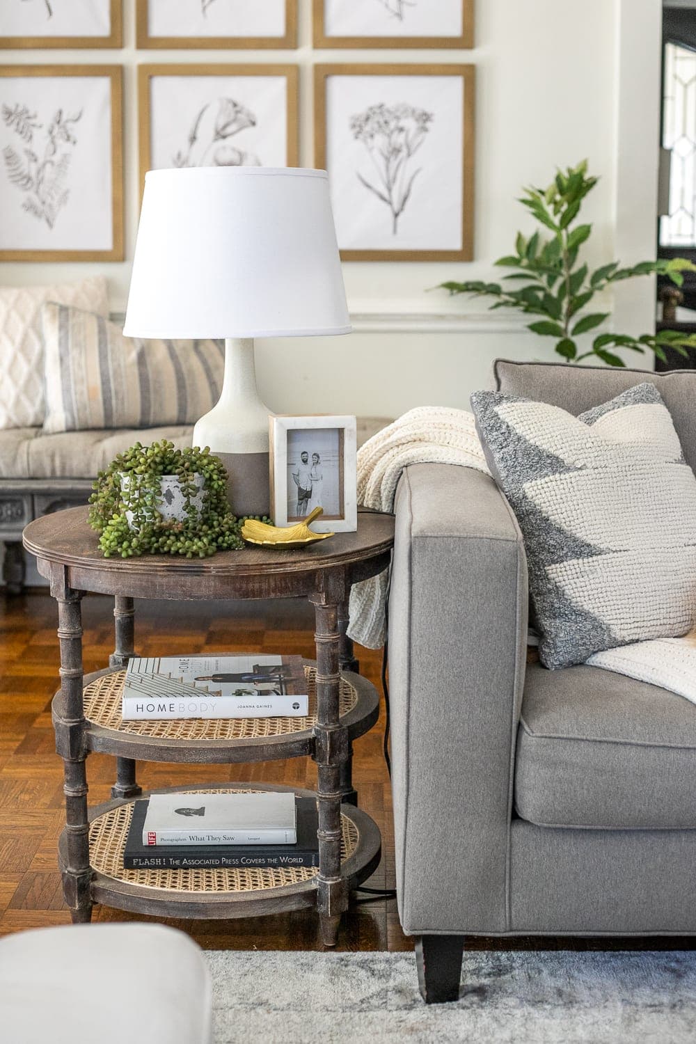 a coffee table beside a grey couch with a lamp, photo frame, and faux plant on it.