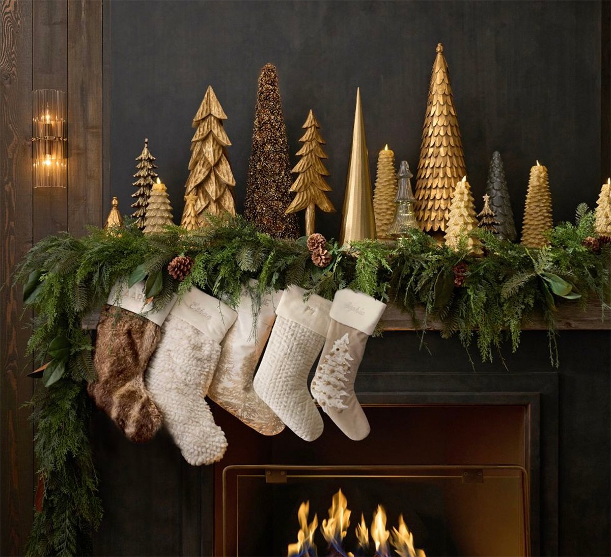 garland hung over a lit fire with stockings and gold christmas trees on the mantel