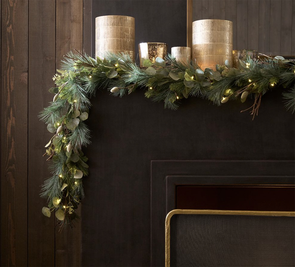 faux pre-lit eucalyptus and pine garland draped over black fireplace with gold candles on the mantel