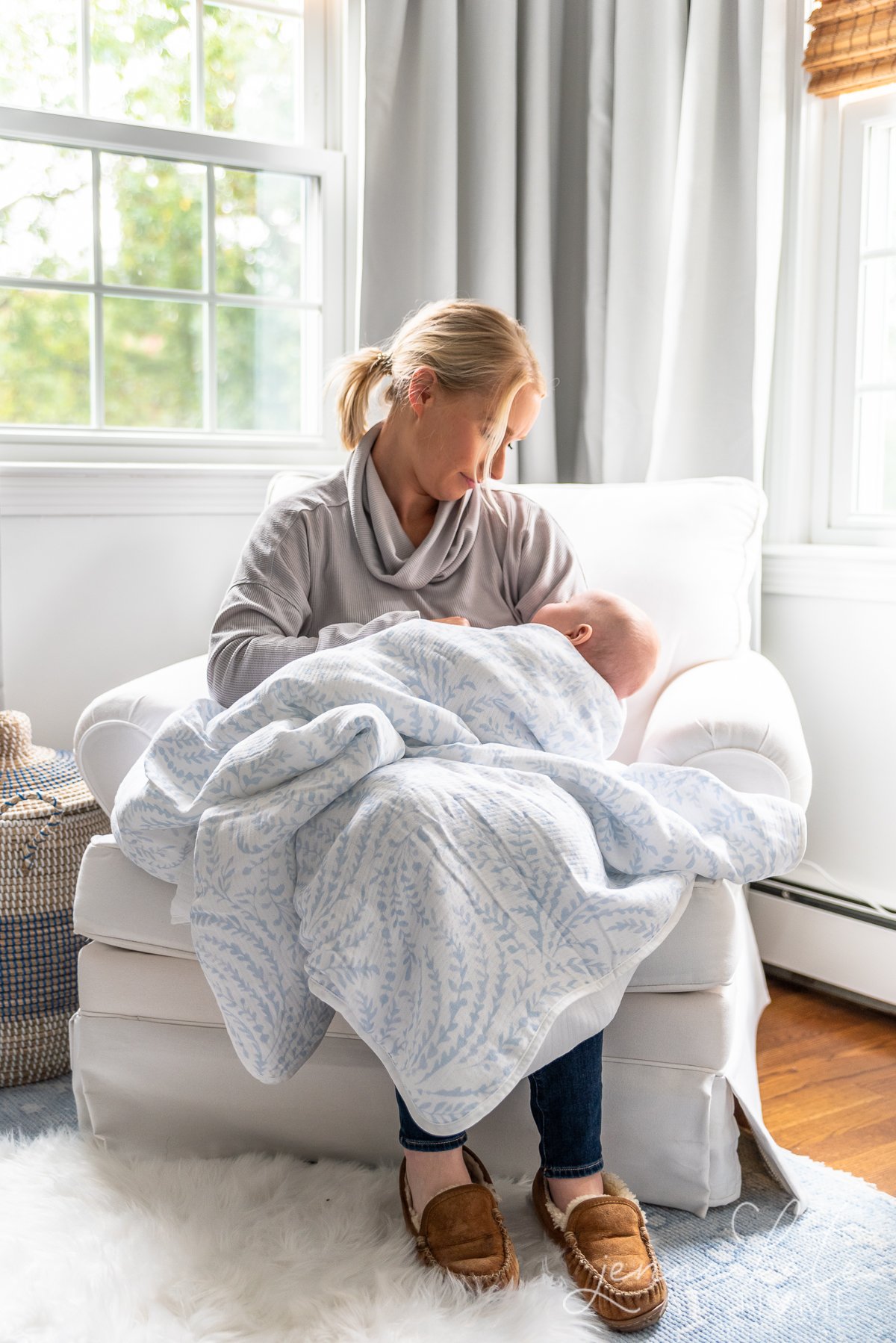 woman sitting in a nursery glider holding a baby draped in a serena & lily muslin blanket