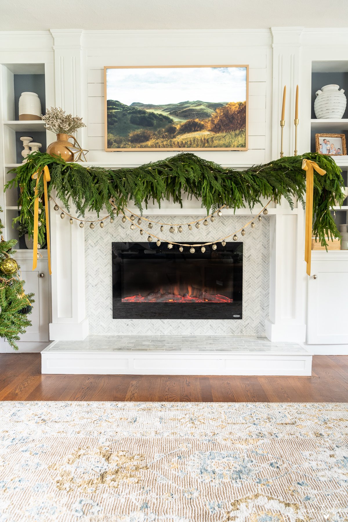 fireplace with thick green garland, gold ribbon and tv over the mantel