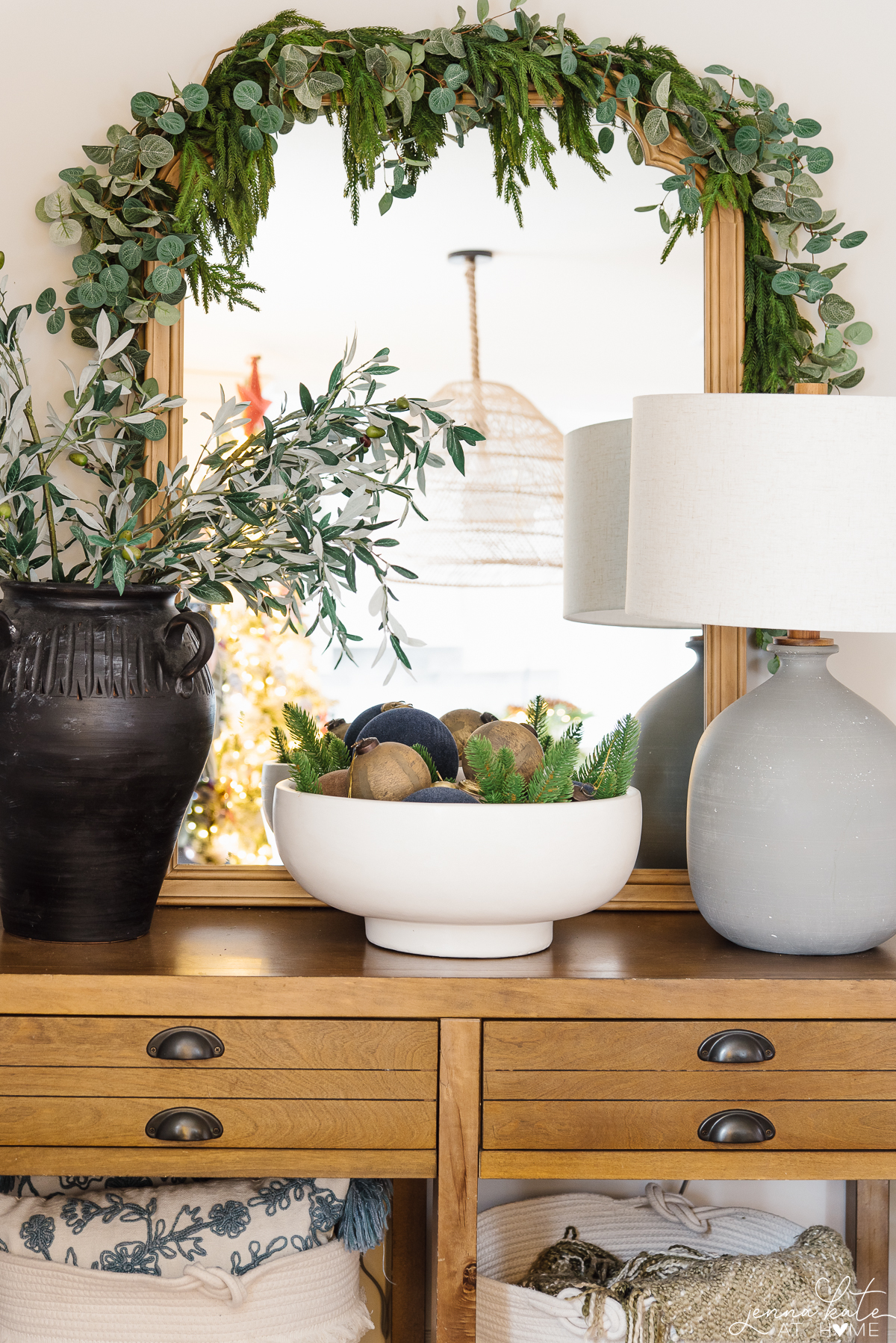 console table with a mirror and a bowl filled with ornaments and faux greenery